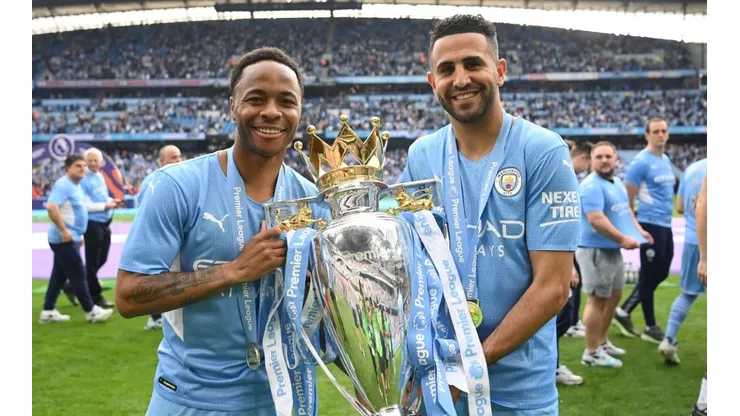 Raheem Sterling and Riyad Mahrez of Manchester City celebrate with the Premier League trophy after their side finished the season as Premier League champions during the Premier League match between Manchester City and Aston Villa at Etihad Stadium on May 22, 2022 in Manchester, England.