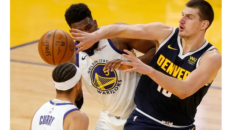 Nikola Jokic (Denver) passing the ball between Stephen Curry and Kevon Looney (Warriors). (Getty)