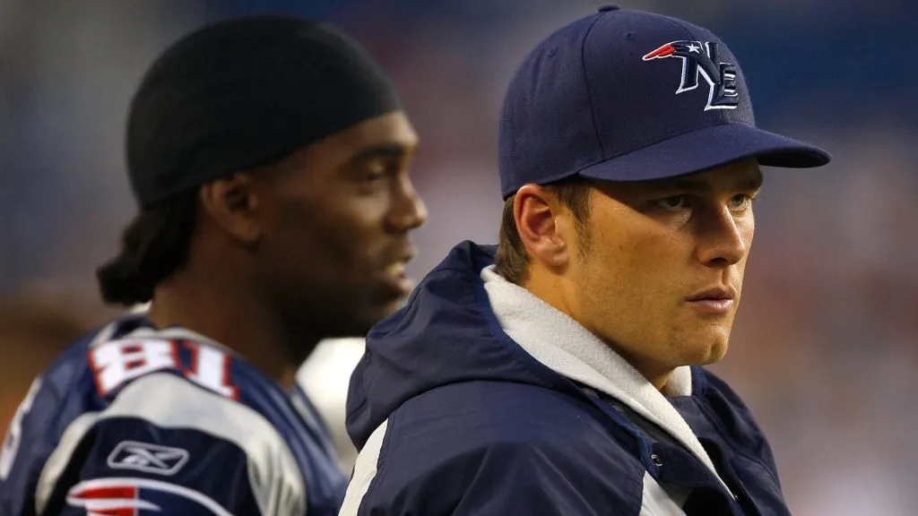 Randy Moss #81 and Tom Brady #12 of the New England Patriots watch the game on the sidelines against the Baltimore Ravens during a preseason game at Gillette Stadium on August 7, 2008 in Foxboro, Massachusetts.