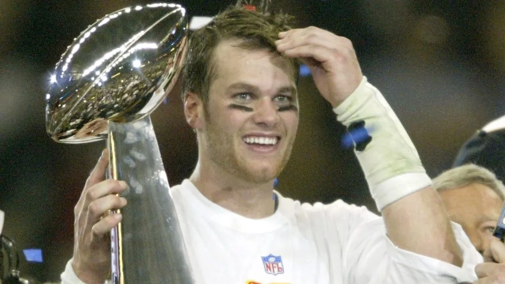 Tom Brady #12 of the New England Patriots raises the Lombardi trophy as he is interviewed by Jim Nance after defeating the Carolina Panthers 32-29 in Super Bowl XXXVIII. (Source: Elsa/Getty Images)