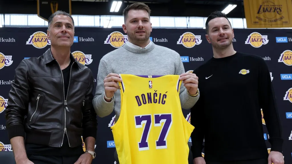 Luka Doncic of the Los Angeles Lakers holds his new jersey while standing alongside general manager Rob Pelinka and head coach JJ Redick during a press conference. (Harry How/Getty Images)
