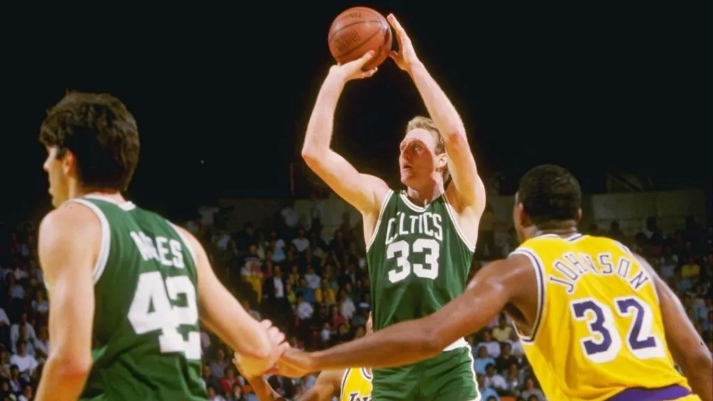 Larry Bird of the Boston Celtics shoots the ball as Magic Johnson of the Los Angeles Lakers watches.