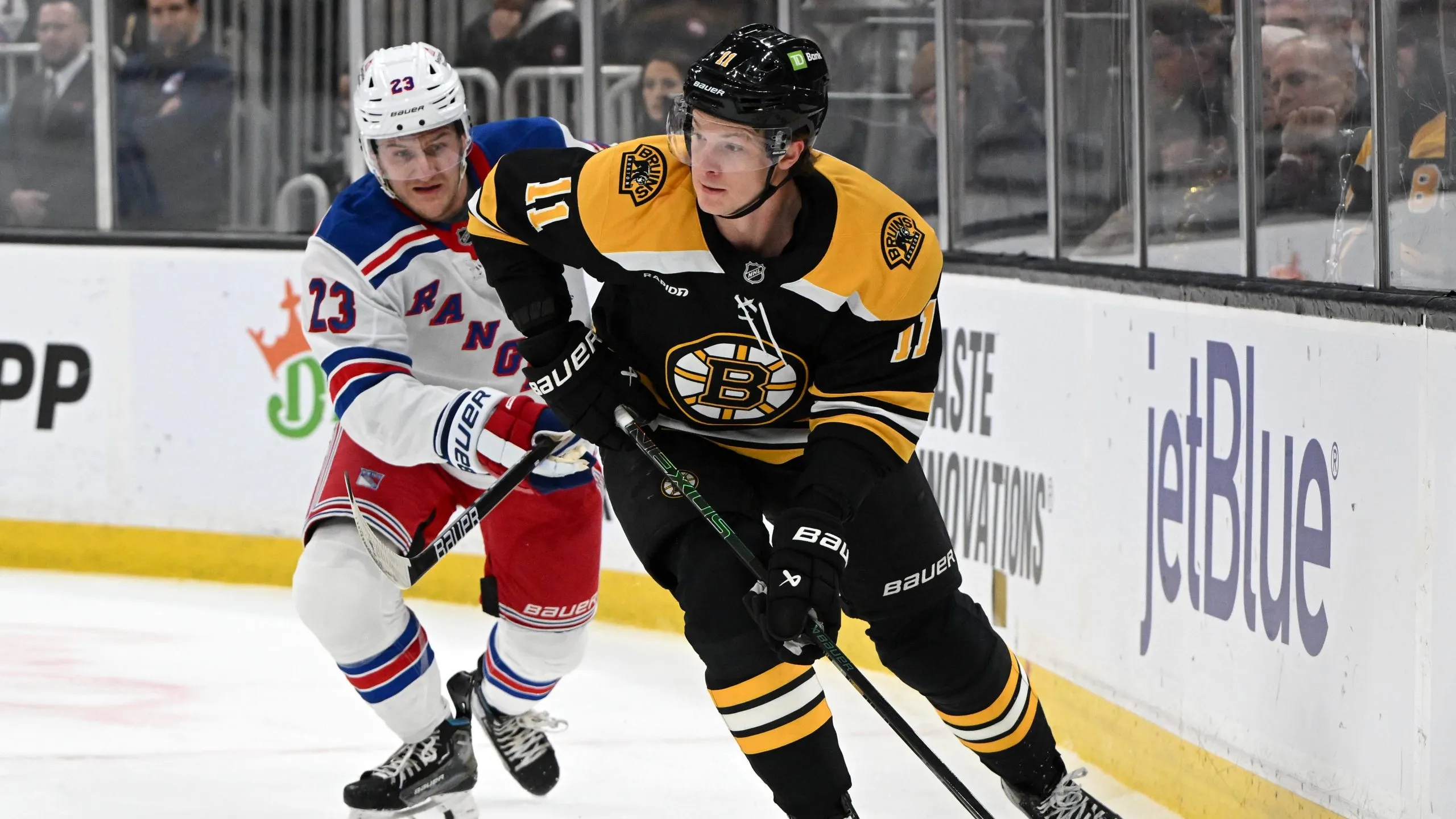 BOSTON, MASSACHUSETTS – FEBRUARY 01: Trent Frederic #11 of the Boston Bruins skates the puck away from Adam Fox #23 of the New York Rangers during the first period at the TD Garden on February 01, 2025 in Boston, Massachusetts. (Photo by Brian Fluharty/Getty Images)