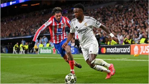 Vinicius Junior of Real Madrid runs with the ball whilst under pressure from Rodrigo De Paul of Atletico de Madrid