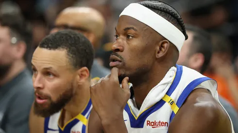 Jimmy Butler III #10 and Stephen Curry #30 of the Golden State Warriors watch from the bench during the second half of the NBA game against the Phoenix Suns at PHX Arena on April 08, 2025 in Phoenix, Arizona.