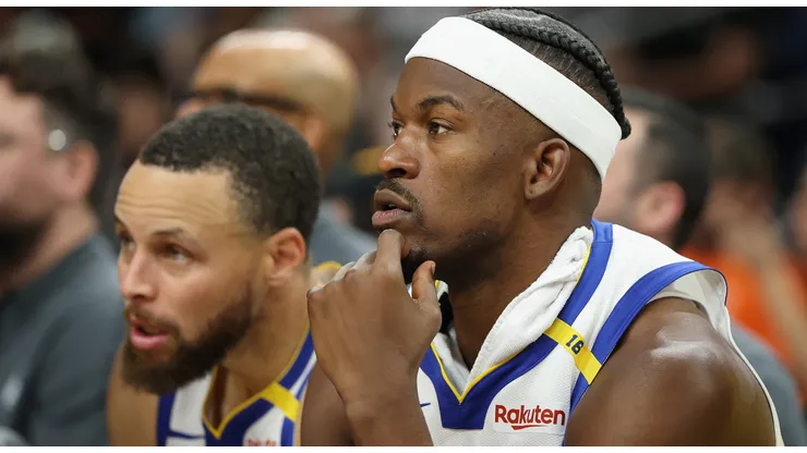 Jimmy Butler III #10 and Stephen Curry #30 of the Golden State Warriors watch from the bench during the second half of the NBA game against the Phoenix Suns at PHX Arena on April 08, 2025 in Phoenix, Arizona.