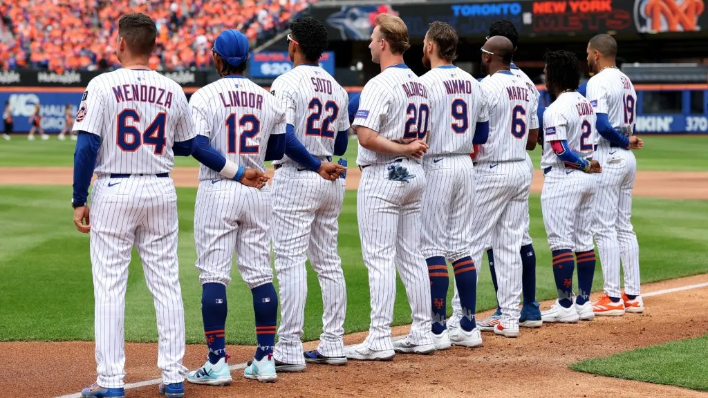 Manager Carlos Mendoza #64 of the New York Mets and the starting lineup for opening day stand for the national anthem before the home opener against the Toronto Blue Jays at Citi Field on April 04, 2025 in the Flushing neighborhood of the Queens borough of New York City. (Photo by Elsa/Getty Images)