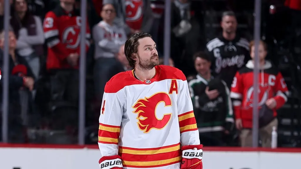 Rasmus Andersson #4 of the Calgary Flames stand on the ice before the game between the New Jersey Devils and the Calgary Flames at Prudential Center on March 20, 2025 in Newark, New Jersey.