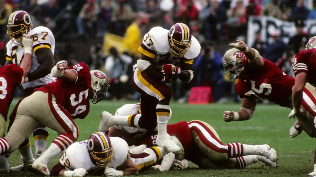 Gerald Riggs of the Washington Redskins runs with the ball under pressure from Matt Millen and Kevin Fagan of the San Francisco 49ers during the 1990 NFC Divisional Playoffs. (Source: George Rose/Getty Images)