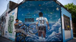 BUENOS AIRES, ARGENTINA - OCTOBER 21: A man wheelies past a mural depicting Diego Armando Maradona entering heaven with a legend that reads in spanish "Here rests god" making reference to the fact that the idol is buried one block away from the mural in Bella Vista on October 21, 2021 in Buenos Aires, Argentina. Football fans all over the country remember their late idol, who would have turned 61 on October 30. (Photo by Tomas Cuesta/Getty Images)