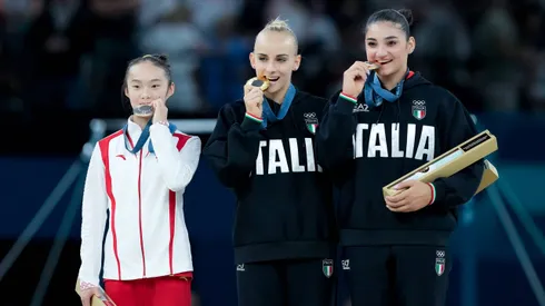 Zhou Yaqin mordiendo la medalla junto a las gimnastas italianas.