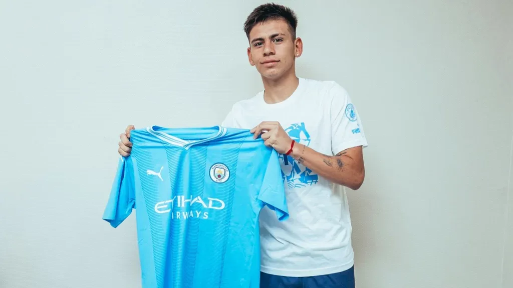 Claudio Echeverri con la camiseta del Manchester City bajo el marco de la firma de su contrato.