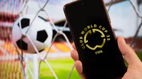 3A0YA55 BOGOTA, COLOMBIA – MARCH 05 OF 2025 A male hand holding a smartphone with fifa club world cup golden logo and blurred football ball at background