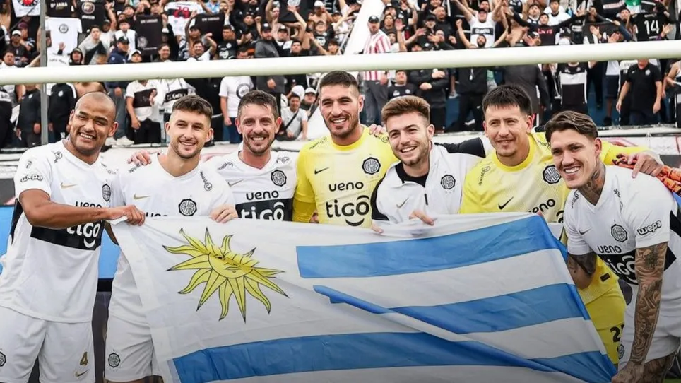 Oliveira, ubicado en el medio, posa con la bandera de Uruguay tras el título de Olimpia (@guaranewsPY).