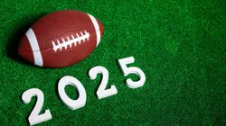 2YHA5NG American football ball next to 2025 number whose figures are made of white painted wood isolated over green grass seen from above.