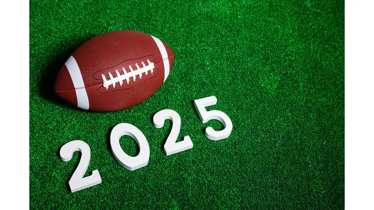 2YHA5NG American football ball next to 2025 number whose figures are made of white painted wood isolated over green grass seen from above.