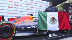 Checo Pérez sostiene la bandera de México al lado de su monoplaza