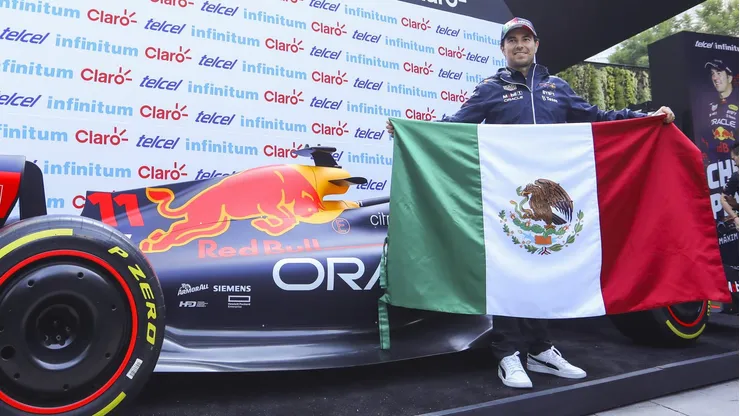Checo Pérez sostiene la bandera de México al lado de su monoplaza