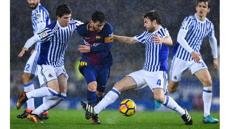 NO LO PUEDEN PARAR. Lionel Messi bajo la lluvia y ante dos jugadores de la Real Sociedad (Foto: Getty).