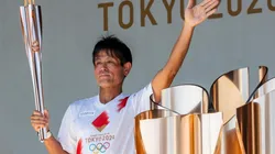 Um dos carregadores da tocha olímpica posa empunhando-a e acenando durante evento em Tóquio (Foto: Getty Images)