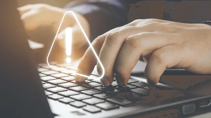 Imagem parcial de homem a trabalhar em laptop, com sinal de perigo sobre o teclado