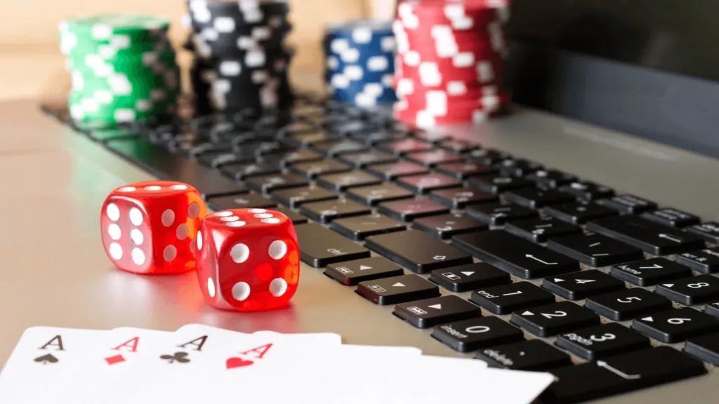 Foto de cartas de baralho, dados e fichas de cassino em cima do teclado de um notebook, representando a seção de cassino das casas de apostas. 