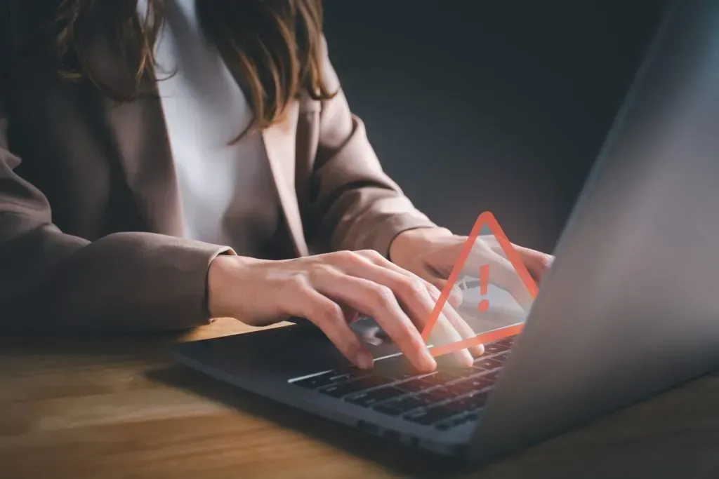 Imagem parcial de mulher a trabalhar em laptop, com sinal de perigo sobre o teclado