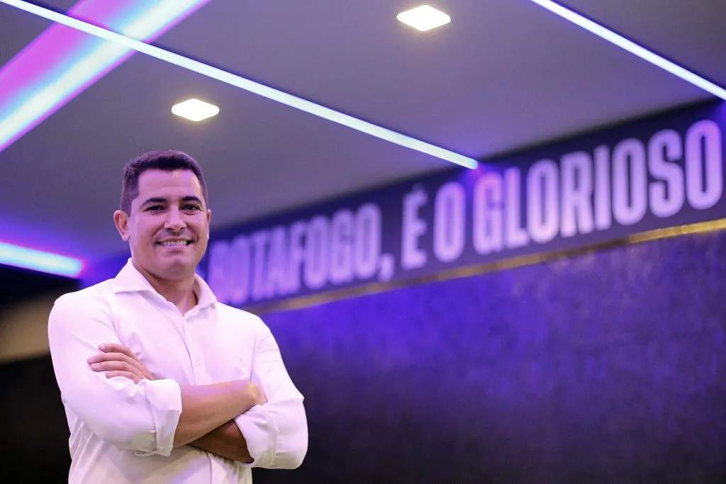 Pedro Martins de braços cruzados sorrindo com escudo do Botafogo ao fundo - Foto: Vitor Silva/Botafogo.