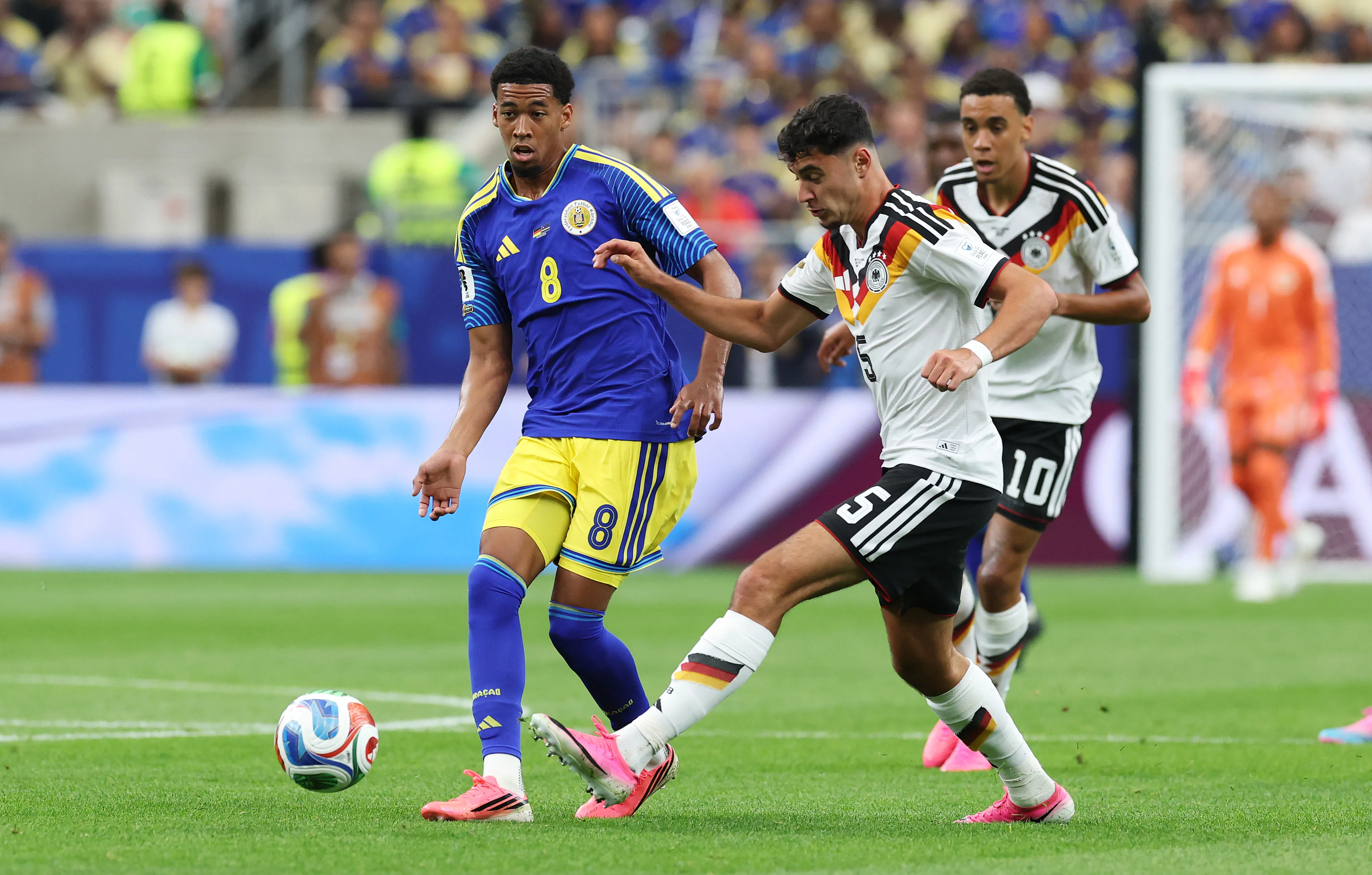 HOUSTON, TEXAS – JUNE 14: Livano Comenencia #8 of Curacao passes against Aleksandar Pavlovic #5 of Germany during the FIFA World Cup 2026 Group E match between Germany and Curacao at Houston Stadium on June 14, 2026 in Houston, Texas. (Photo by Alexander Hassenstein/Getty Images)